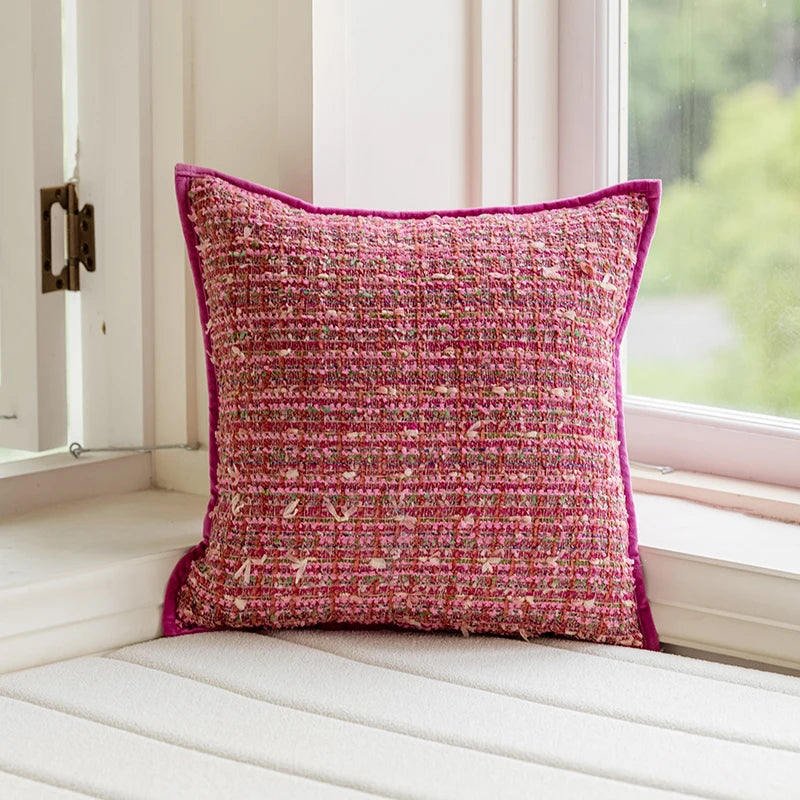 Pink textured pillow on a white window seat with a blurred green outdoor background