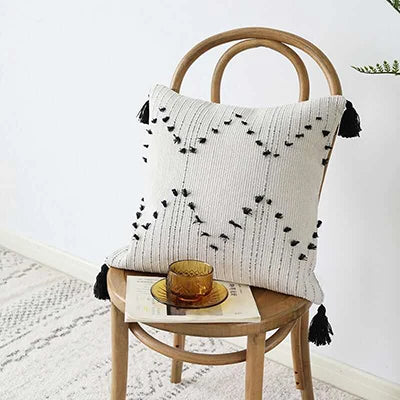 Decorative pillow with black patterns and tassels on a wooden chair with a white background