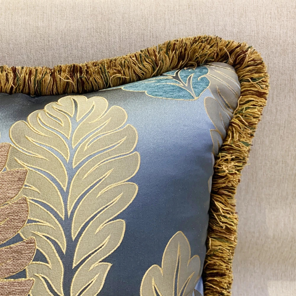 Decorative pillow with leaf pattern and gold trim on a neutral background