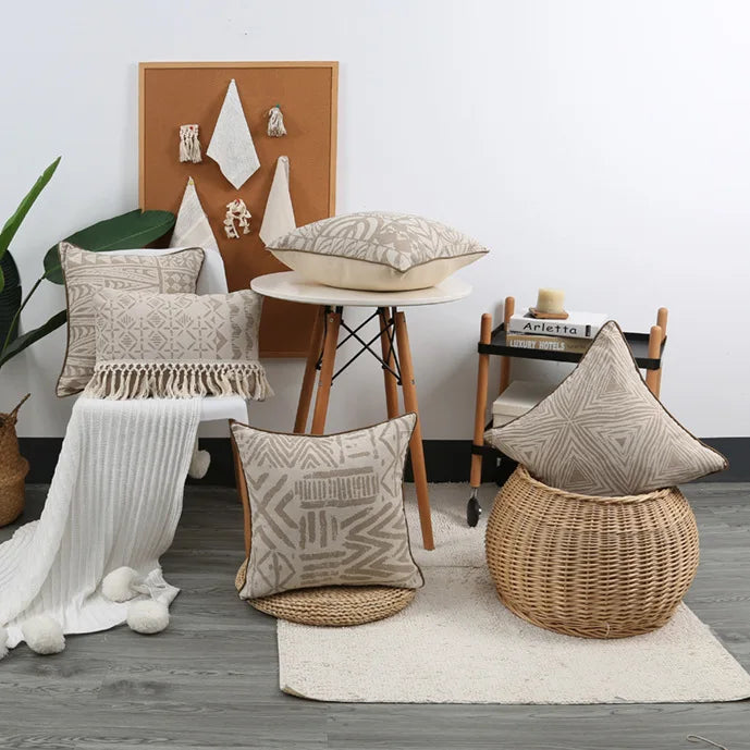 Decorative pillows and a woven stool in a room with a white wall and wooden floor.