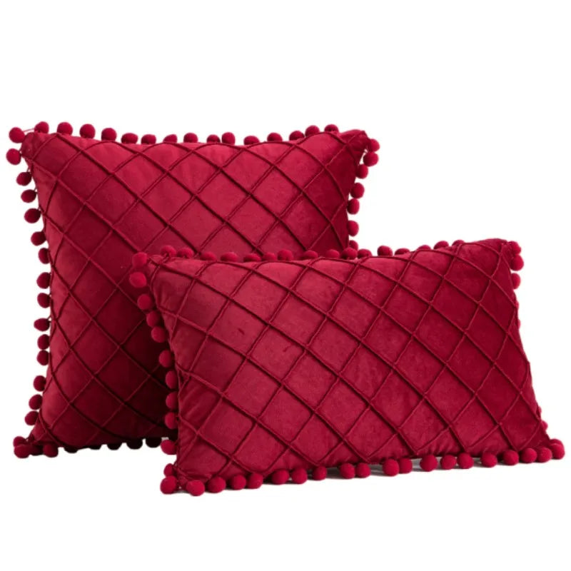 Two red textured pillows with pom-pom trim on a white background