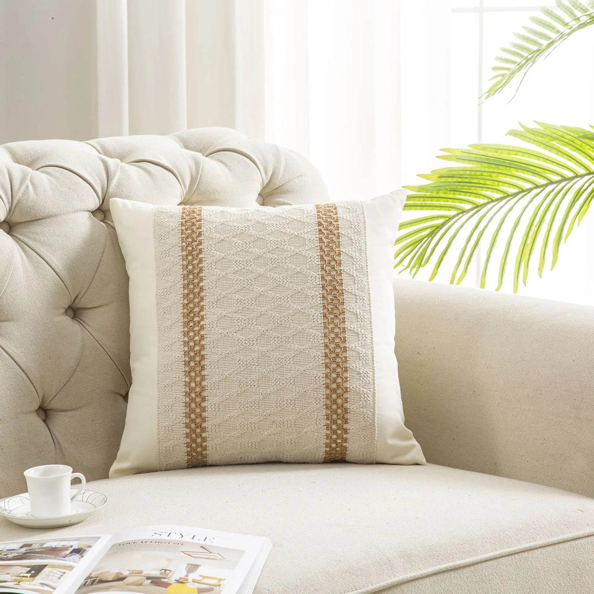 Decorative pillow on a beige sofa with a cup and magazine in the foreground, and a blurred green plant in the background.