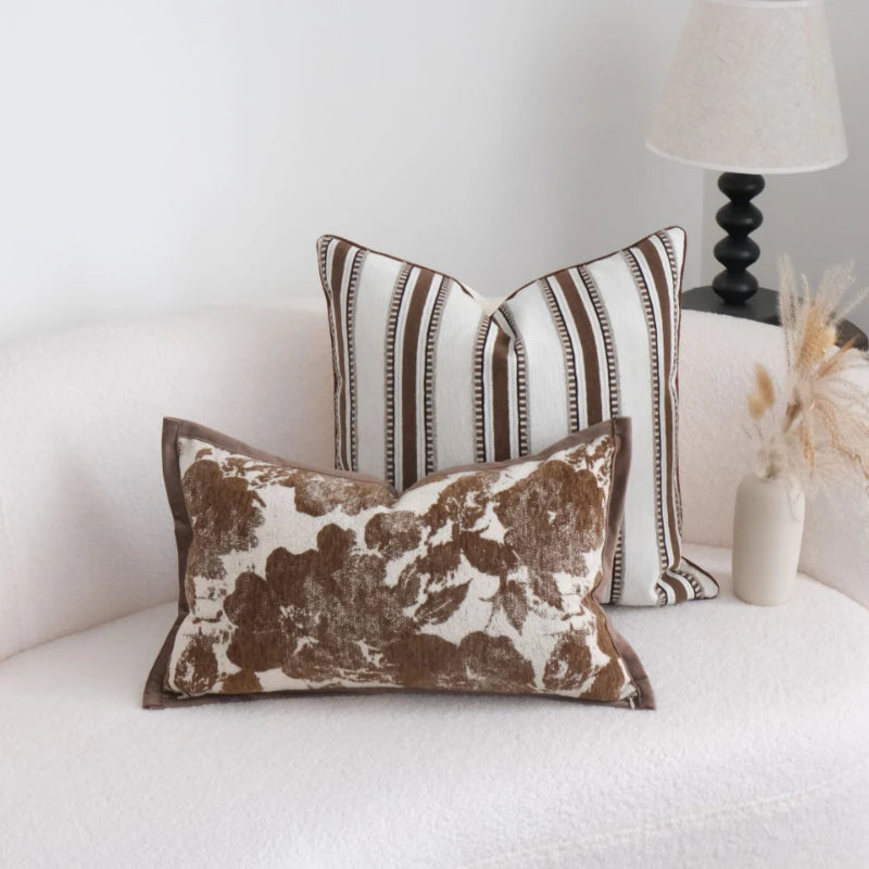 Two decorative pillows on a white couch with a lamp and vase in the background.