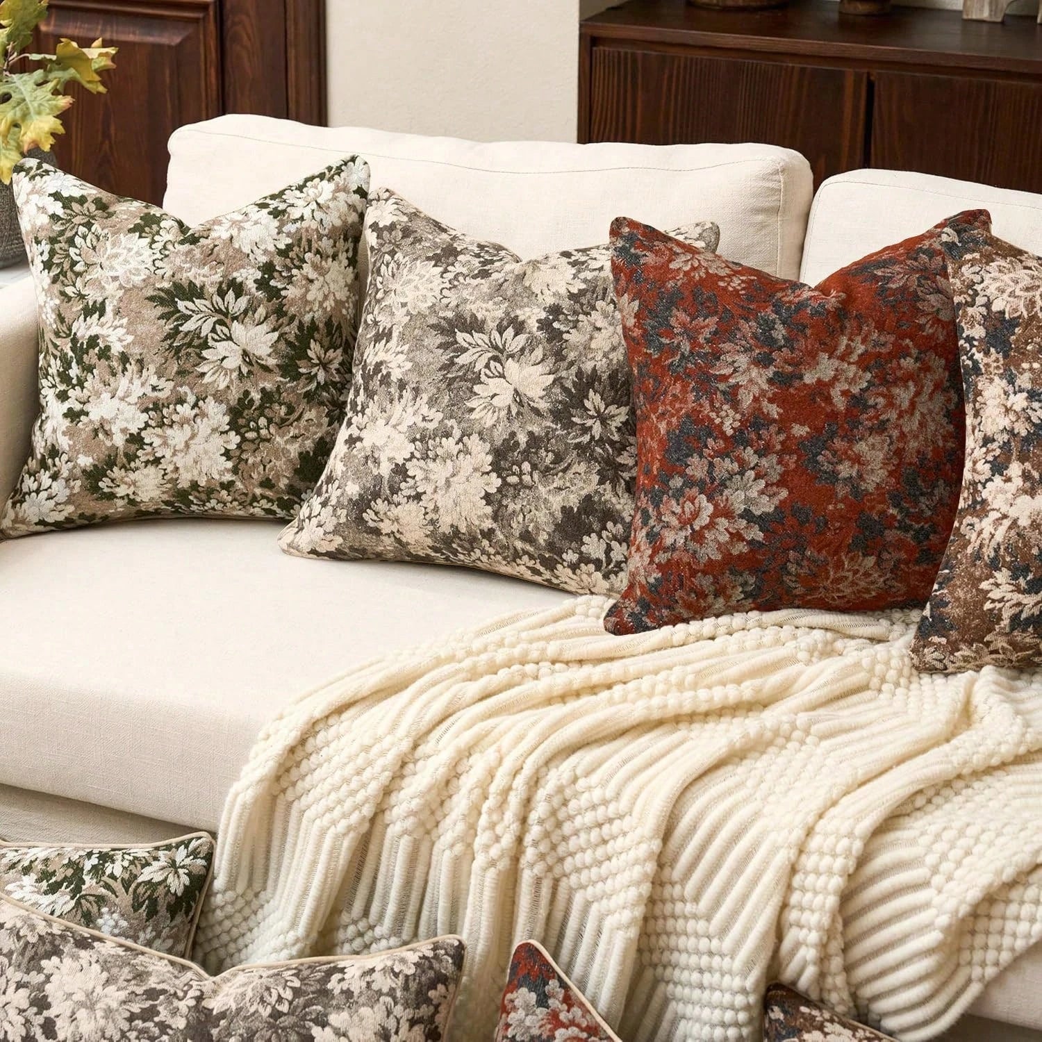 Decorative pillows on a sofa with a floral and patterned design, featuring a blanket draped over the armrest.
