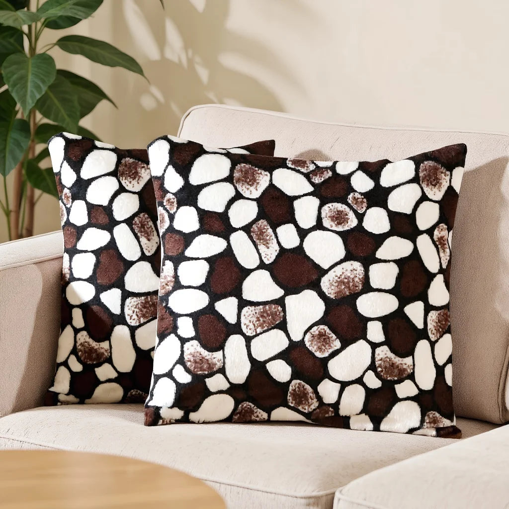 Two patterned pillows on a beige sofa with a plant in the background
