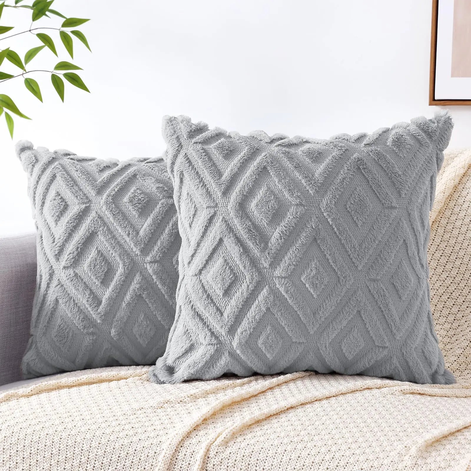 Two gray textured pillows on a beige couch with a white wall and plant in the background.