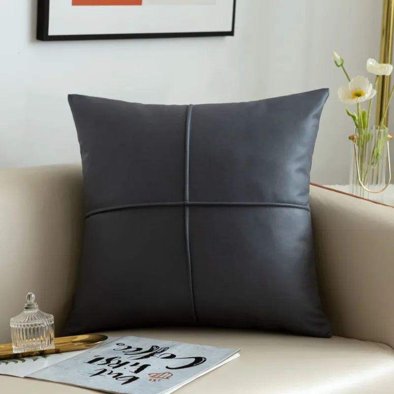 Gray leather pillow on a beige sofa with a decorative frame and flowers in the background