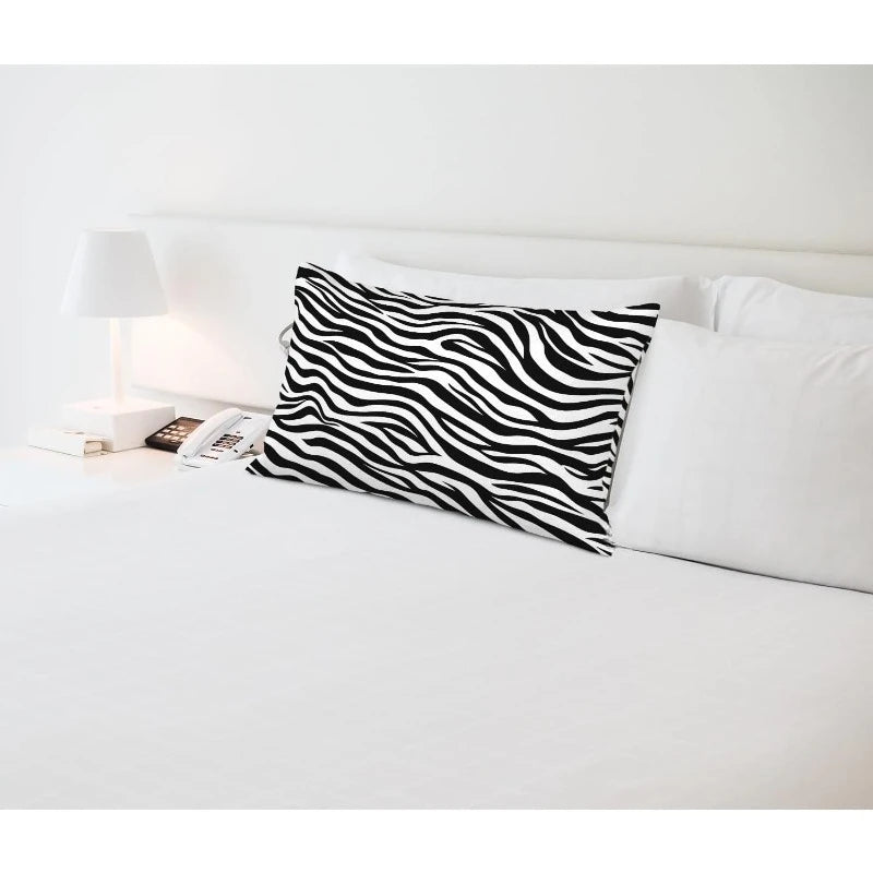 Zebra-striped pillow on a bed with white bedding and a lamp in the background.