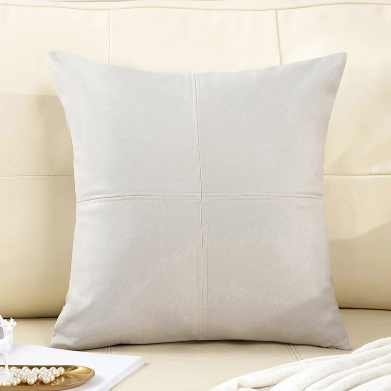 Beige leather pillow on a beige sofa with a white blanket and jewelry tray.
