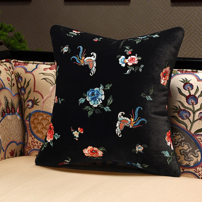 Decorative pillow with floral and butterfly patterns on a black background, placed on a couch.
