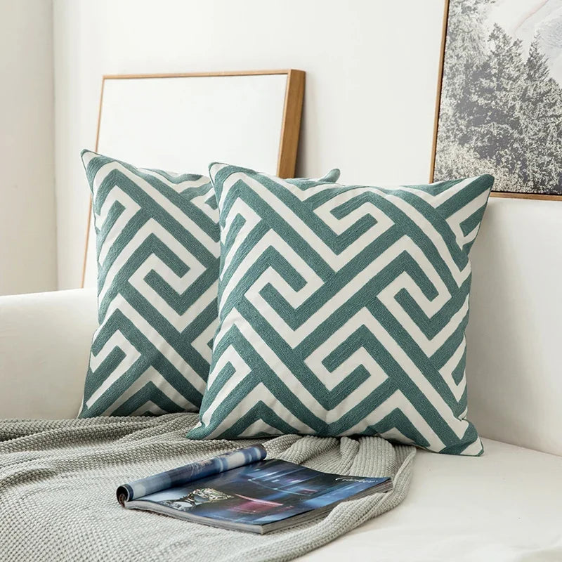 Two green and white patterned pillows on a couch with a magazine underneath.