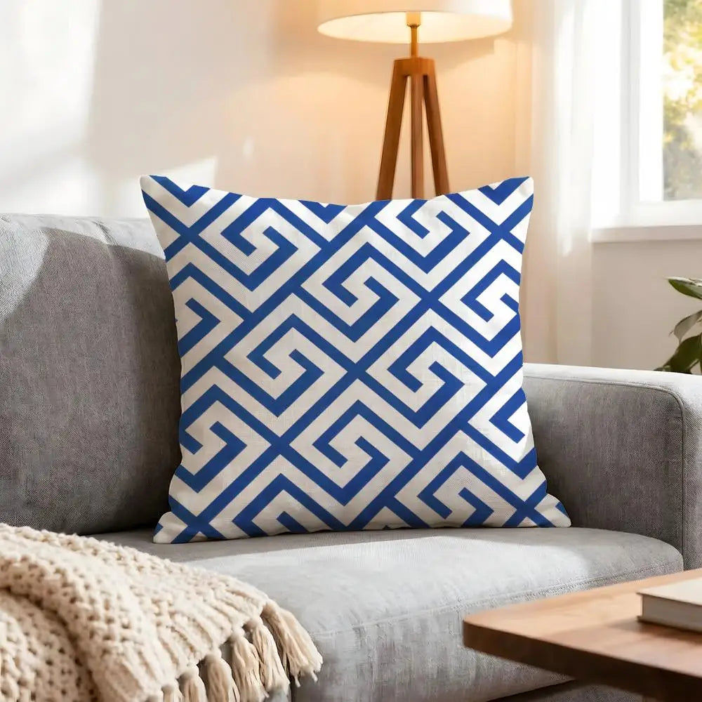 Blue and white patterned pillow on a gray sofa with a lamp and table in the background.
