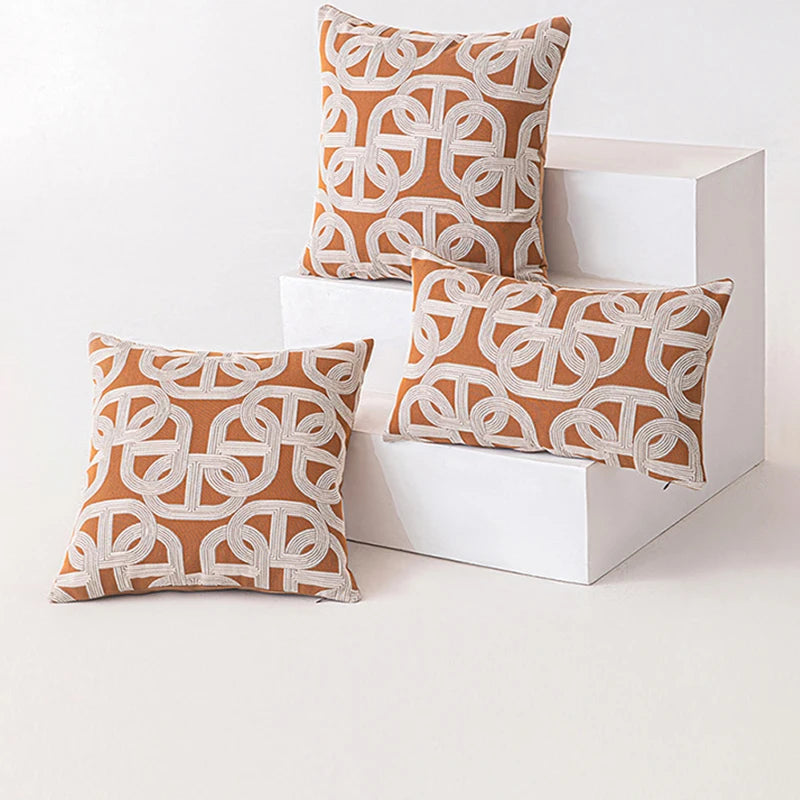 Three orange and white patterned pillows on a white surface