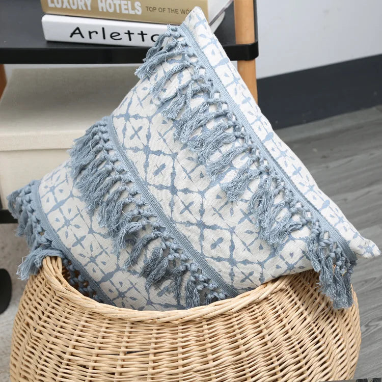 Decorative pillow with blue tassels in a wicker basket on a wooden floor.