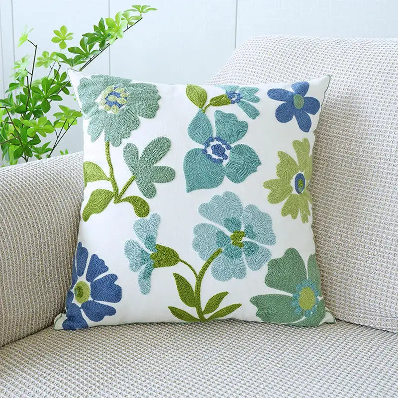 Floral-patterned pillow on a couch with a light blue wall and plant in the background