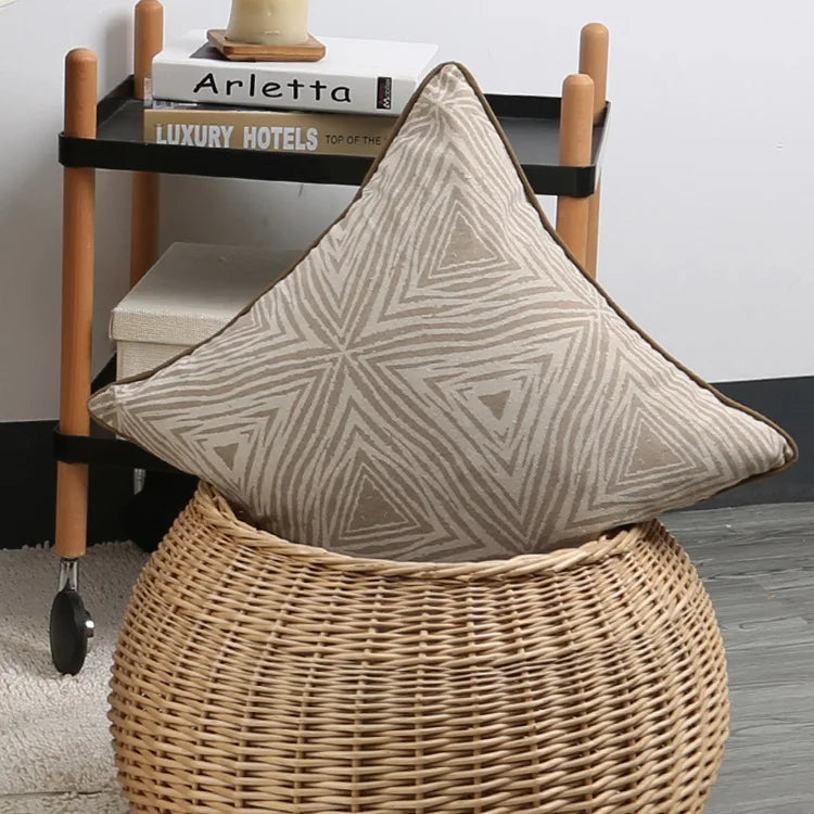Decorative pillow with geometric pattern on a wicker stool in a room setting.