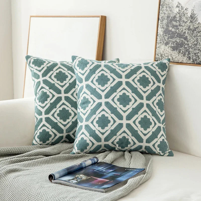 Teal and white patterned pillows on a couch with a magazine and blanket.