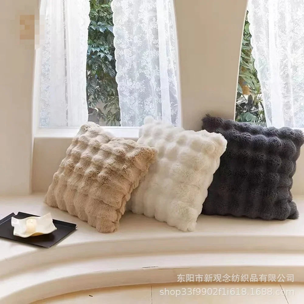 Three textured pillows on a windowsill with white curtains and greenery outside.