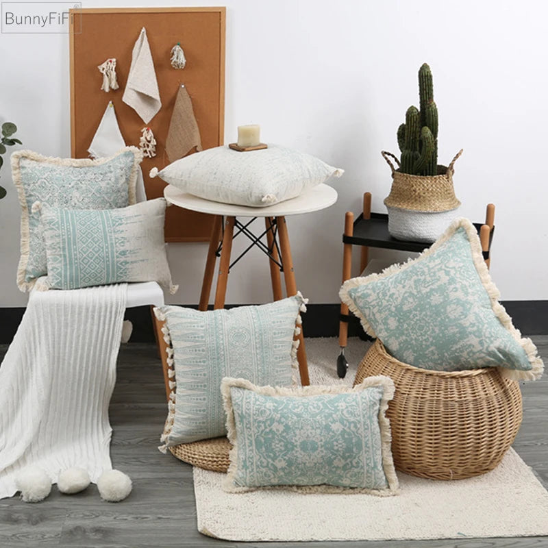 Decorative pillows with tassels on a wooden floor with a table and plant in the background.