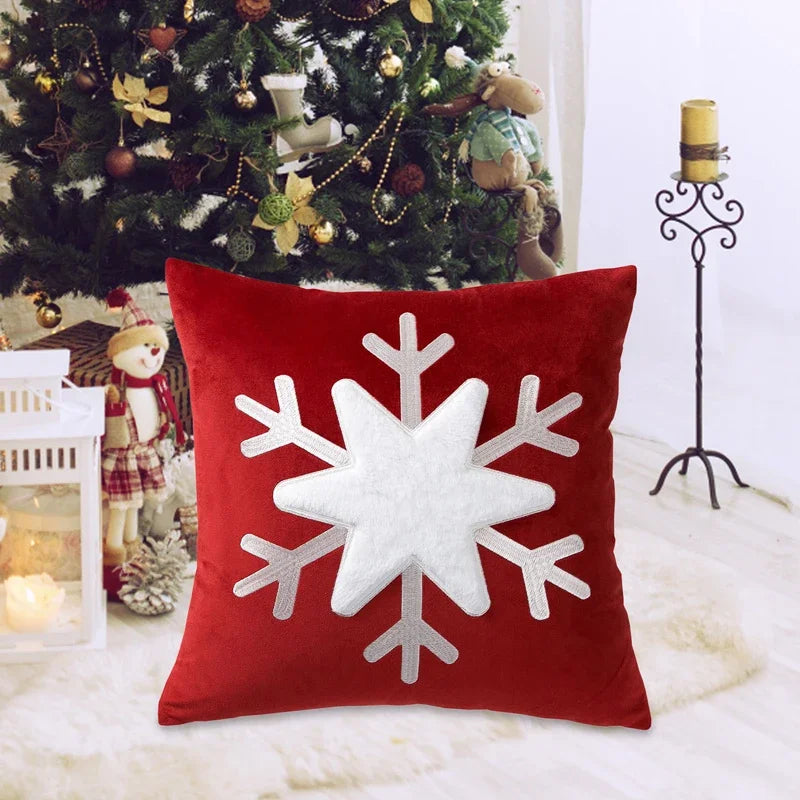 Red pillow with a white snowflake design in front of a decorated Christmas tree.