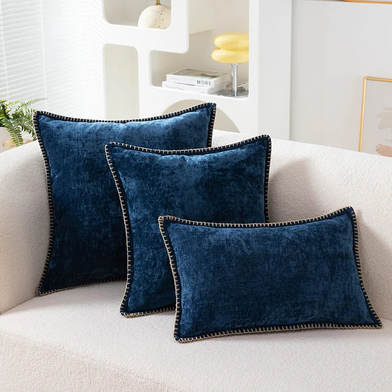Three blue velvet pillows on a white sofa in a living room setting.