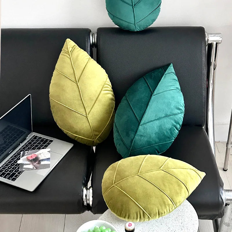 Leaf-shaped cushions in green and yellow on a black chair with a laptop and small table.