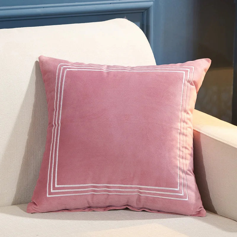 Pink pillow with white trim on a beige couch against a blue wall.