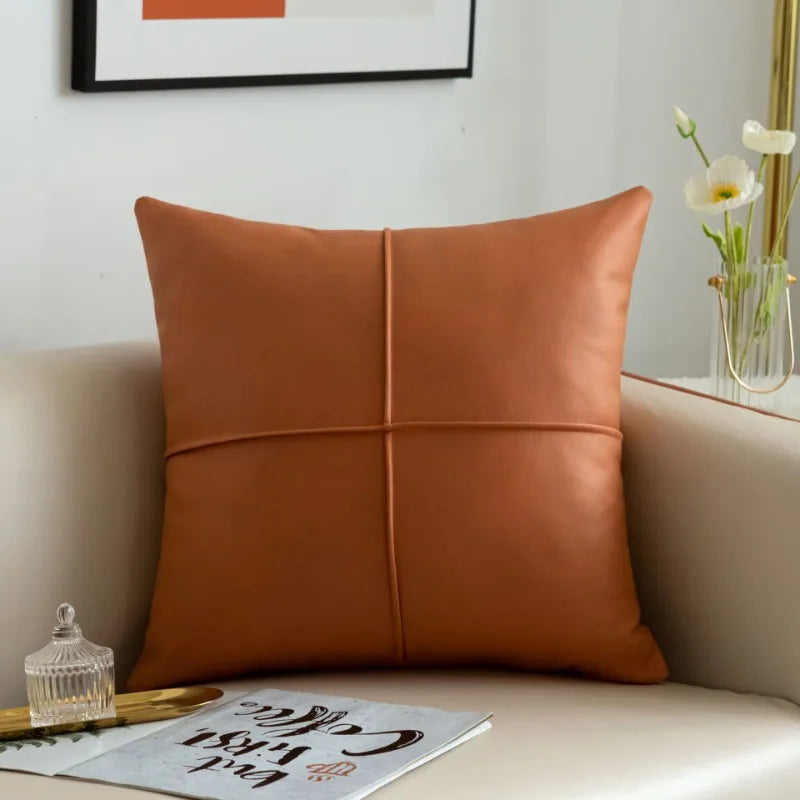 Brown leather pillow on a sofa with a decorative frame and flowers in the background