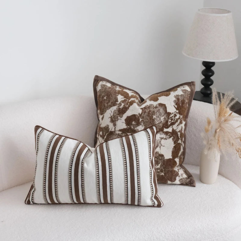 Two decorative pillows on a white couch with a lamp in the background.