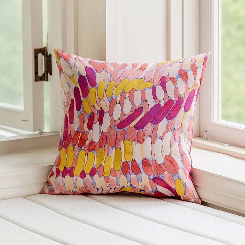 Colorful patterned pillow on a white cushion by a window