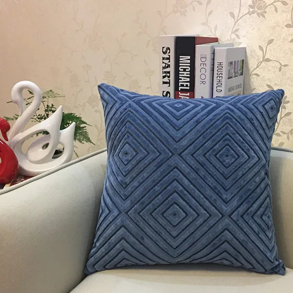 Blue textured pillow on a sofa with decorative books and a plant in the background.