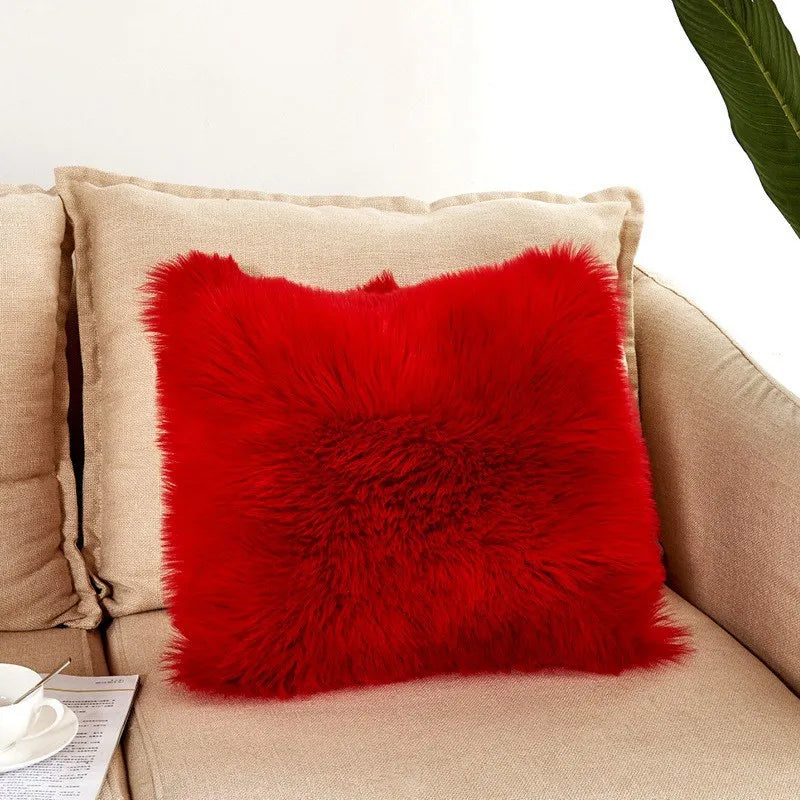 Red fluffy pillow on a beige couch with a white wall background