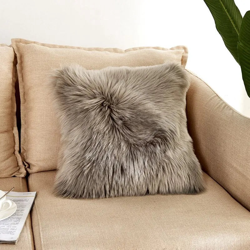Gray fluffy pillow on a beige couch with a plant in the background