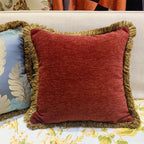 Red pillow with gold fringes on a floral-patterned surface