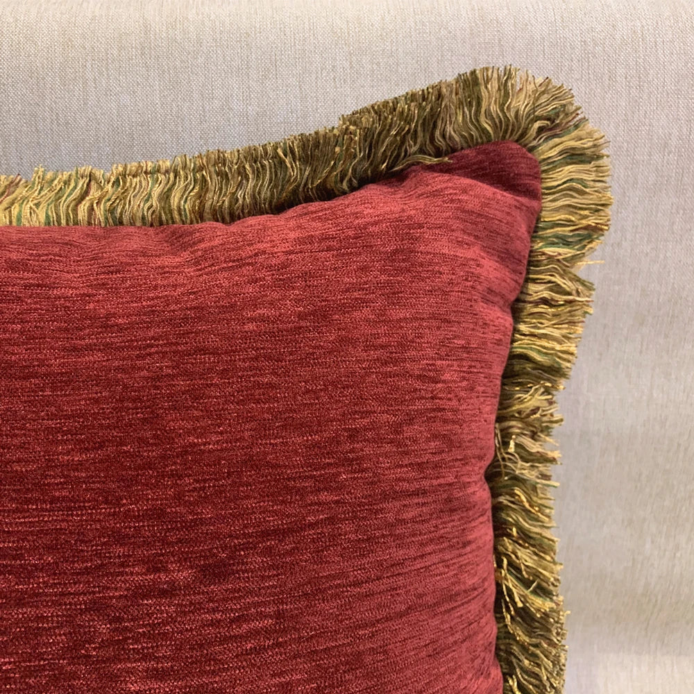 Red textured pillow with gold fringe on a neutral background