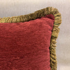 Red textured pillow with gold fringe on a neutral background