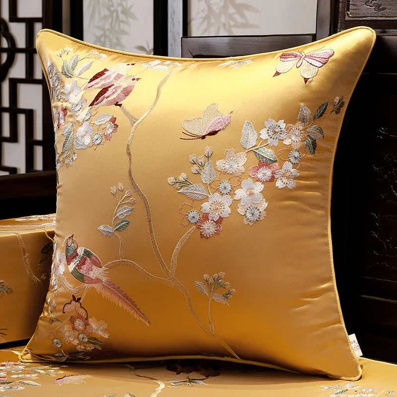 Gold pillow with floral and butterfly embroidery on a wooden surface.