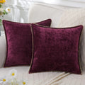 Two purple velvet pillows on a white couch with flowers in the background