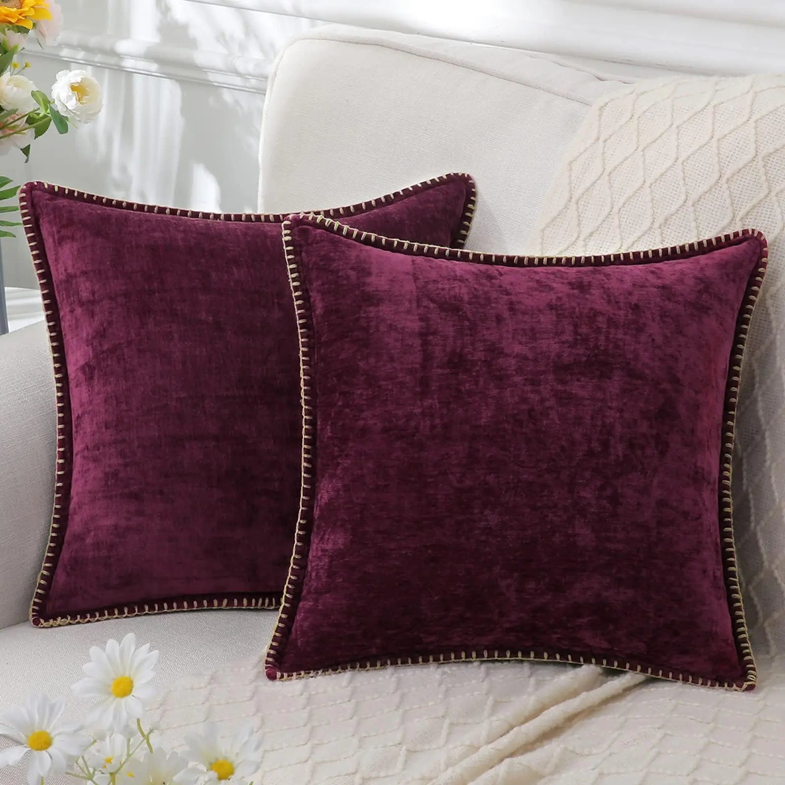 Two purple velvet pillows on a white couch with flowers in the background