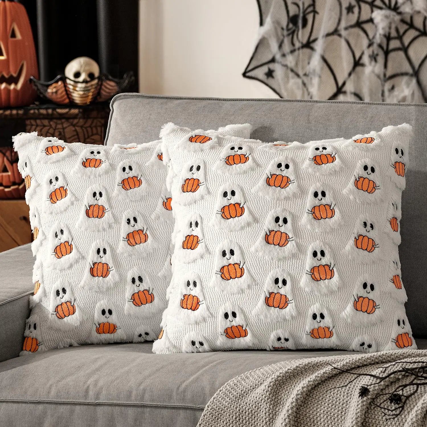 Decorative pillows with ghost and pumpkin pattern on a gray couch, Halloween-themed decor in the background.