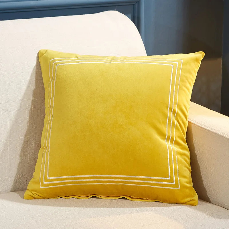 Yellow pillow with white trim on a beige couch against a blue wall
