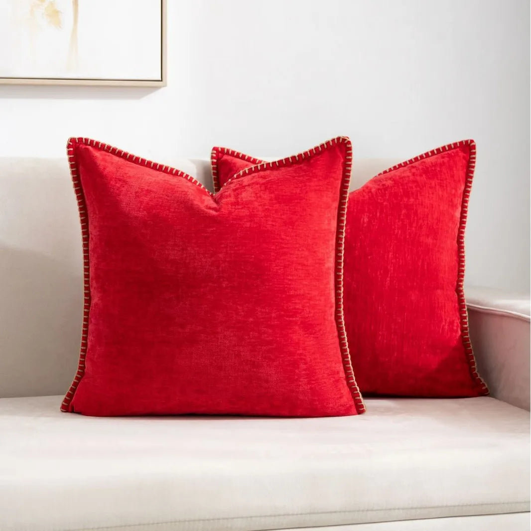 Two red pillows with gold trim on a white couch.