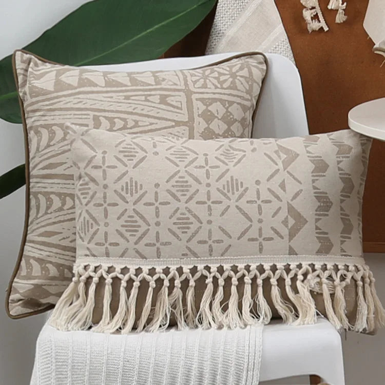 Decorative pillows with geometric patterns and tassels on a white chair.