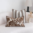 Two decorative pillows on a white couch with a lamp and vase in the background.