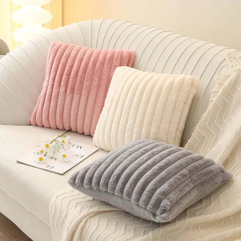 Three textured pillows in pink, beige, and gray on a sofa with a blanket and a magazine.