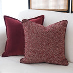 Two red pillows on a white couch with a wicker chair in the background.