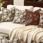 Decorative pillows on a sofa with a floral and patterned design, featuring a blanket draped over the armrest.