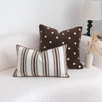 Two decorative pillows, one with brown polka dots and the other with brown stripes, on a white couch.