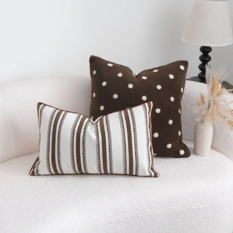 Two decorative pillows, one with brown polka dots and the other with brown stripes, on a white couch.