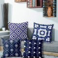 Four blue patterned pillows on a gray sofa with a decorative wall in the background.